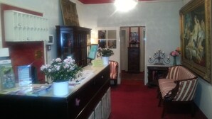 A reception area with a counter, a chair, a cabinet, and a painting on the wall. - Hotel Galleria (Munich)