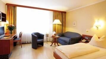 A hotel room with a bed, a desk, a chair, a sofa, and a lamp.