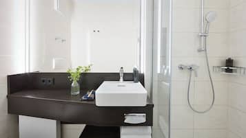 Un baño moderno con tocador de madera oscura, un lavabo blanco, cabina de ducha de vidrio y un perchero para toallas.