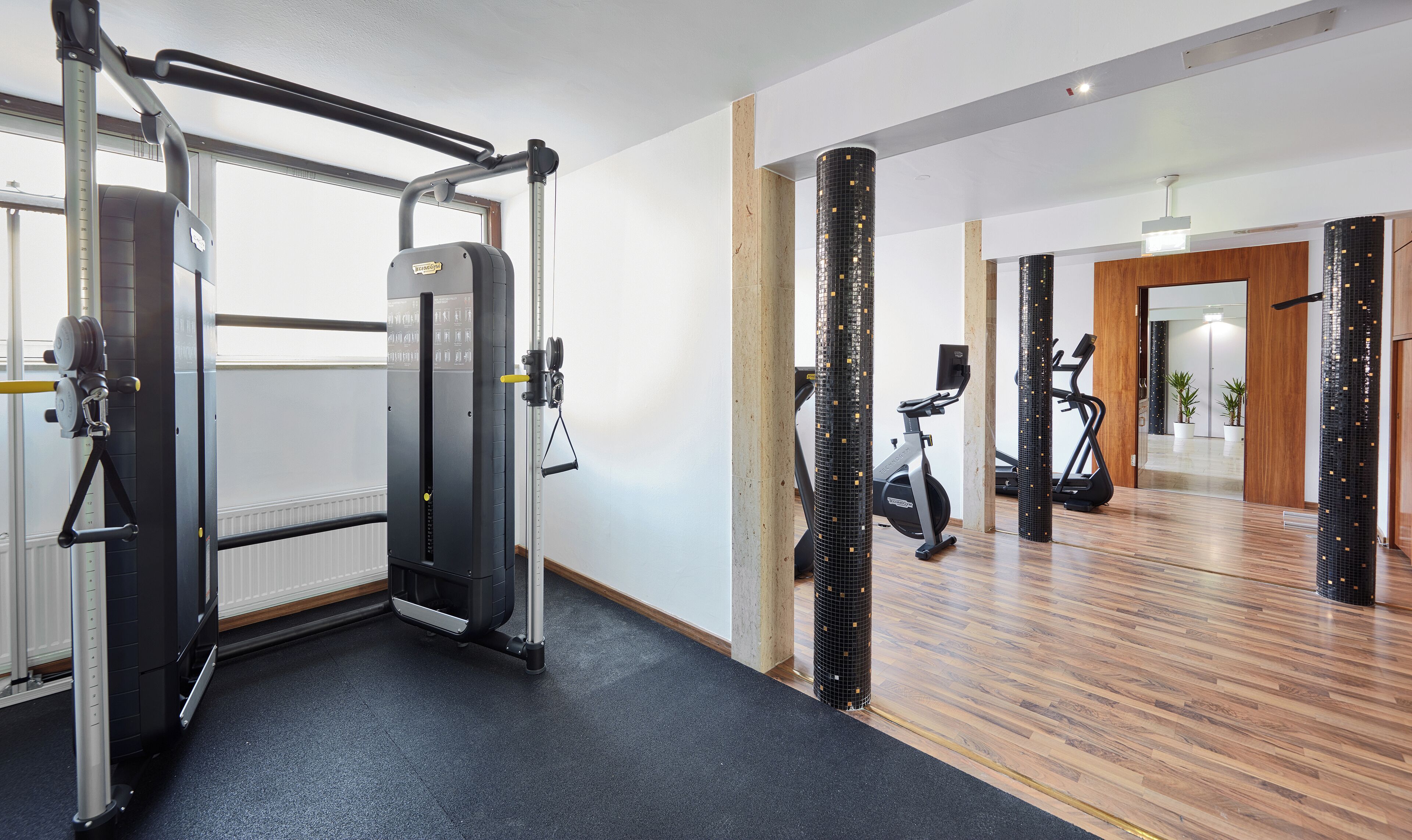 Een sportschool met trainingsapparatuur, een spiegel en een houten vloer.