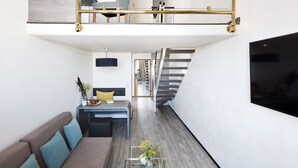 Una habitación de hotel moderna con zona superior, escalera, sofá, escritorio y televisor.