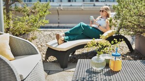 Una persona descansando en un banco con una bebida y una planta sobre una mesa.