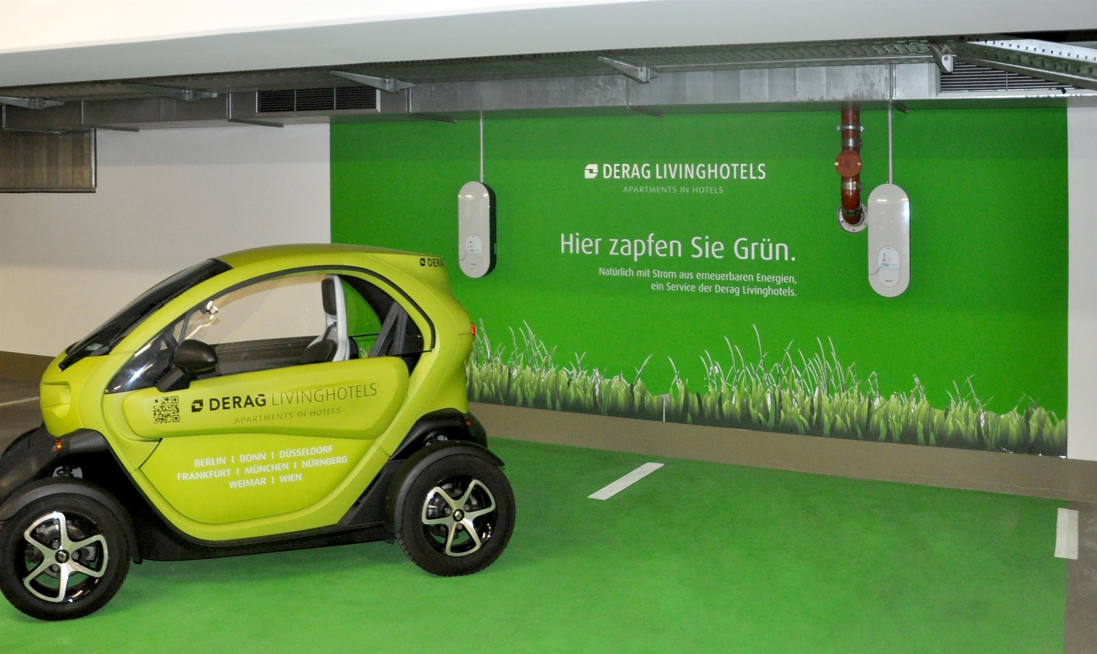 Un vehículo eléctrico compacto y amarillo estacionado en un espacio interior moderno con una pared verde que muestra texto y un código QR.
