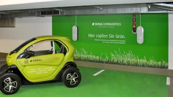 Un vehículo eléctrico compacto y amarillo estacionado en un espacio interior moderno con una pared verde que muestra texto y un código QR.