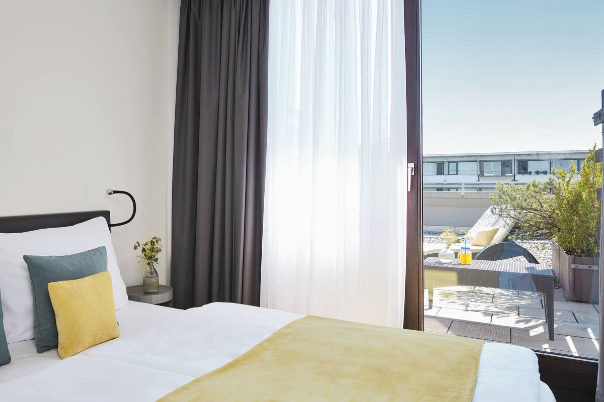 A hotel room with a bed, curtains, and a view of the outside.