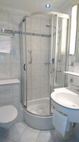 Un baño moderno con ducha de vidrio, inodoro blanco y lavamanos con espejo.
