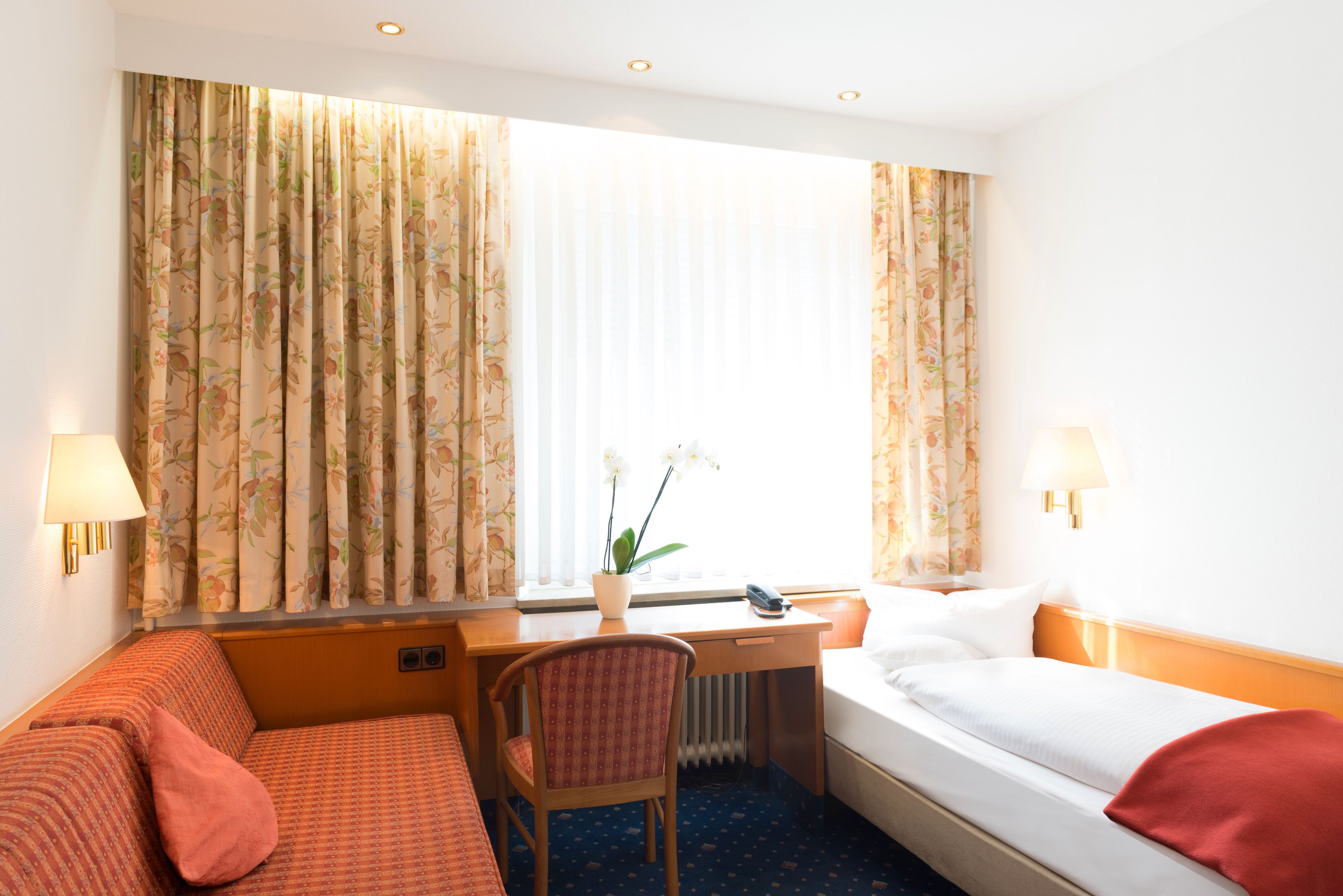 A hotel room with a bed, a desk, a chair, and a window with curtains.