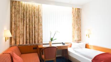 A hotel room with a bed, a desk, a chair, and a window with curtains.
