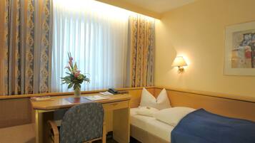 A hotel room with a desk, chair, bed, and a lamp.