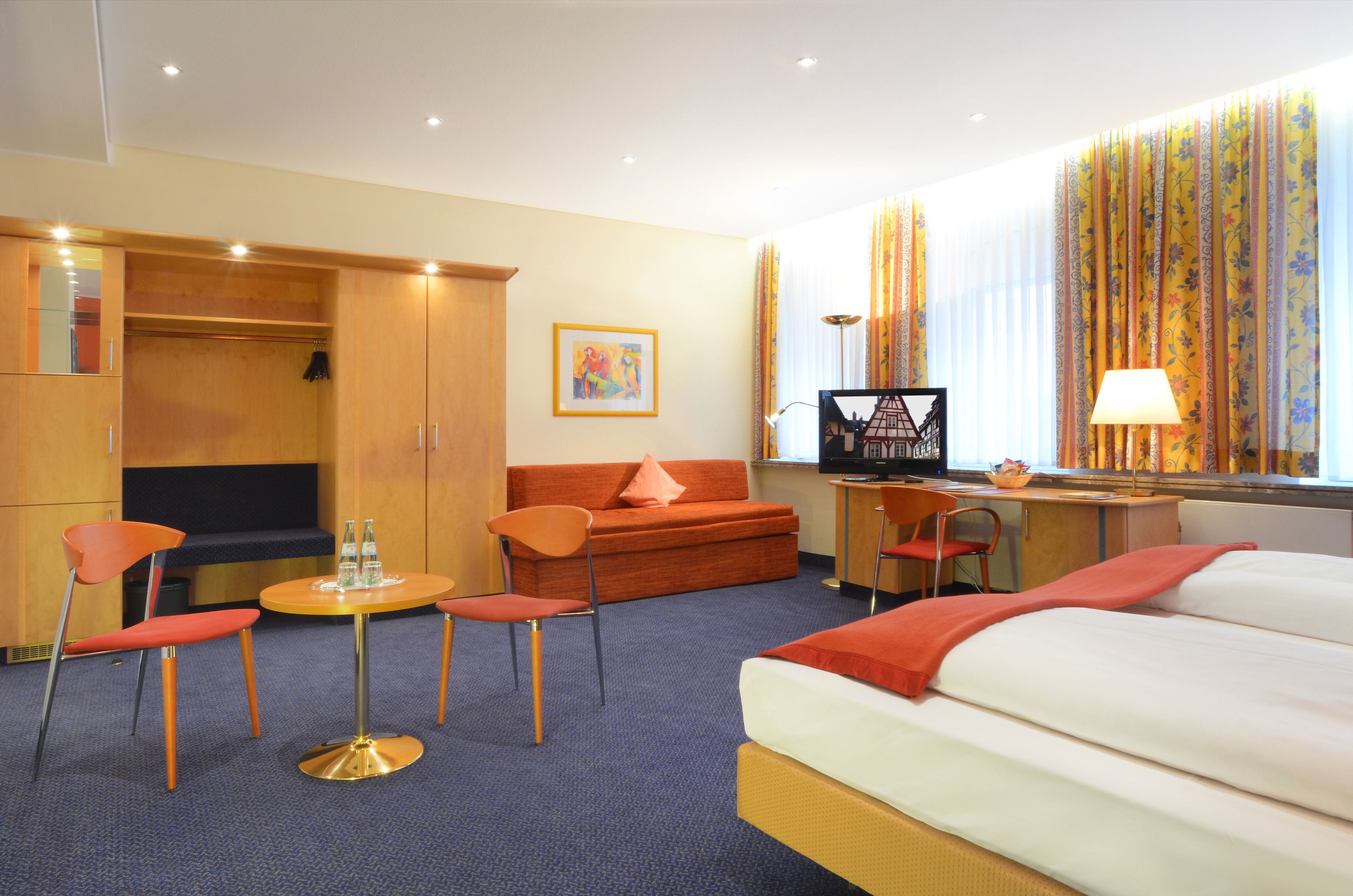 Ein Hotelzimmer mit Bett, Sofa, Schreibtisch, Fernseher und Kleiderschrank.
