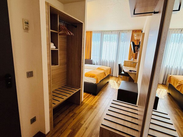 A hotel room with a wooden wardrobe, a bed, a desk, and a chair.