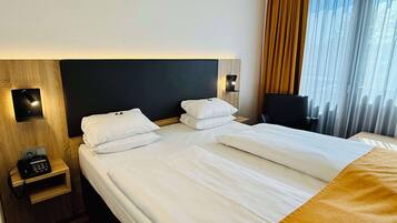 A hotel room with a large bed, a bedside table with a phone, and a window with curtains.