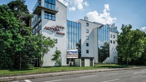 A modern hotel with a prominent glass facade, a rooftop terrace, and a sign reading "Hotel Arvena Messie."