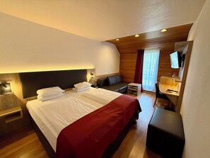 A hotel room with a large bed, a bedside table, a small seating area, a vanity with a mirror, and a television. - Arvena Messe Hotel an der NürnbergMesse (Nuremberg)