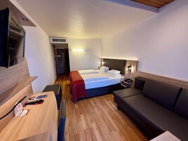Habitación de hotel compacta con cama, escritorio, silla, sofá y televisión.