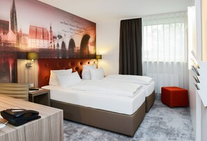 Una habitación de hotel con una cama grande, un escritorio, un teléfono y un pouf rojo.