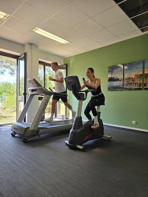 A gym with treadmills and stationary bikes, large windows, and a green wall.