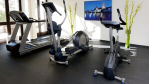 Un gimnasio con máquinas de cardio, un amplio ventanal y un cuadro en la pared.