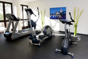Uma academia com aparelhos de cardio, uma janela grande e um quadro na parede.