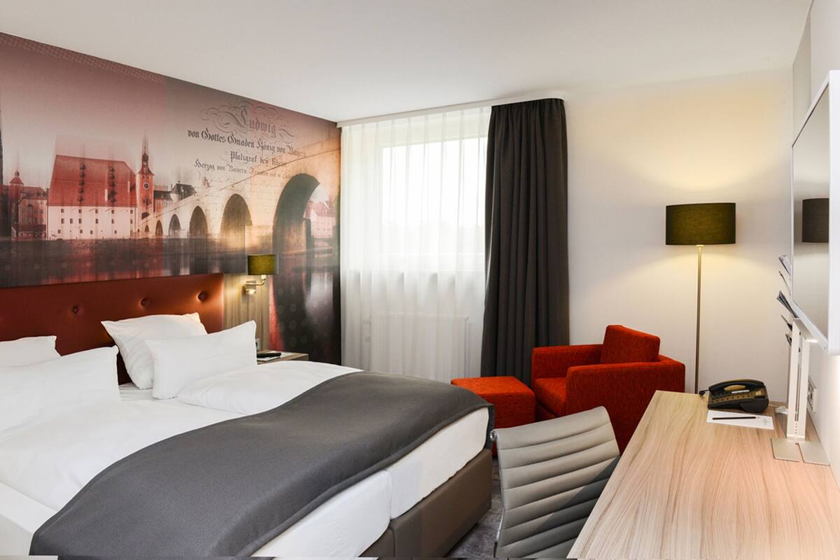 Une chambre d’hôtel avec un grand lit, un bureau, une chaise et une fresque murale.