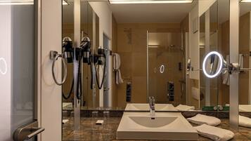 Casa de banho com um espelho grande, duas pias, chuveiro e secador de cabelo.
