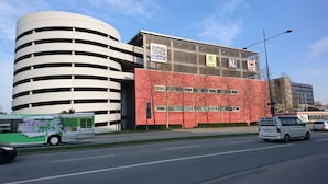 Un edificio moderno con una estructura cilíndrica y fachada roja, que muestra la señalización de 'Donau Einkaufszentrum' y 'EDEKA'.