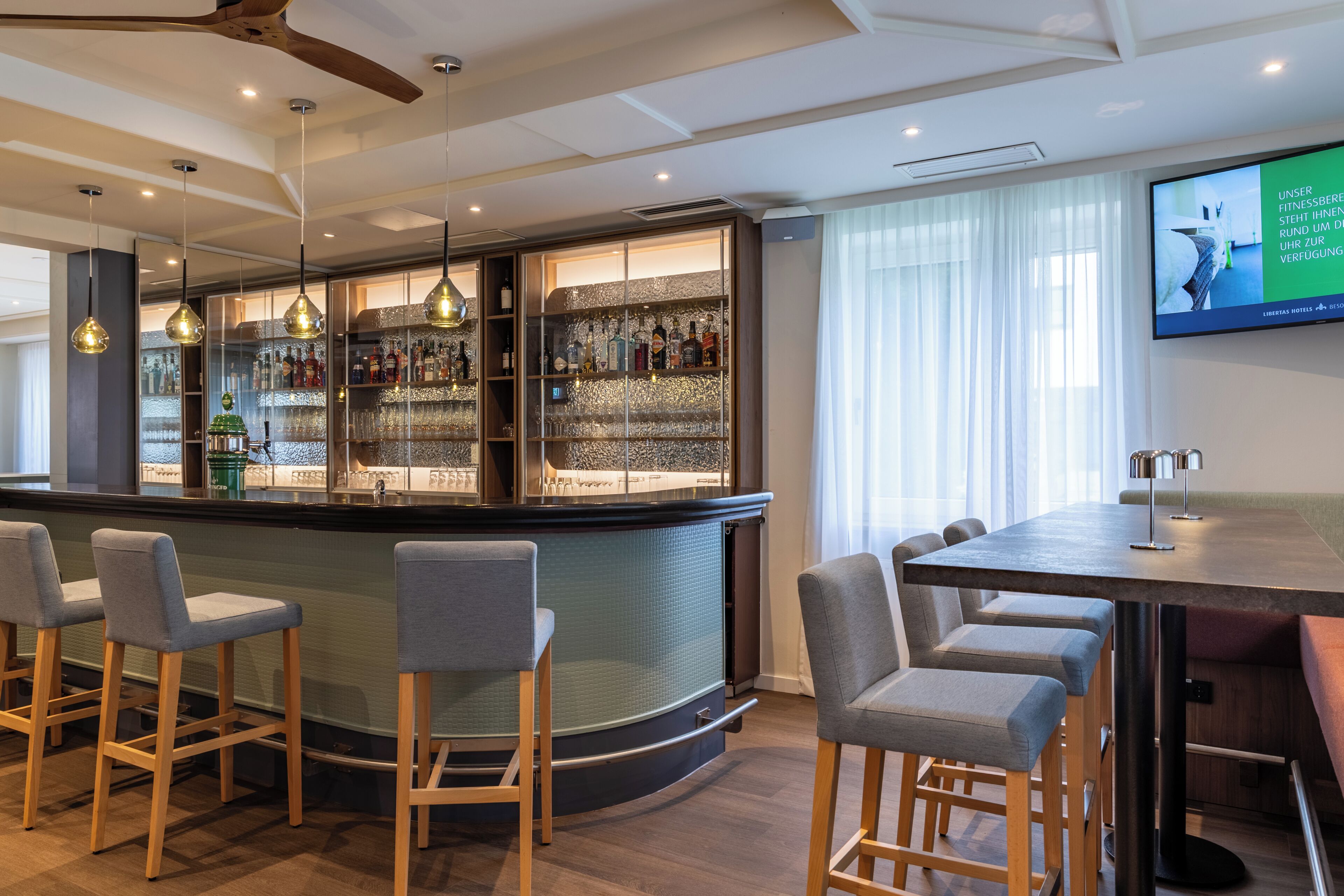 A bar area with a curved counter, bar stools, and a television screen.