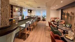 Un moderno vestíbulo de hotel con zona de bar, diferentes disposiciones de asientos y un amplio ventanal con vistas.