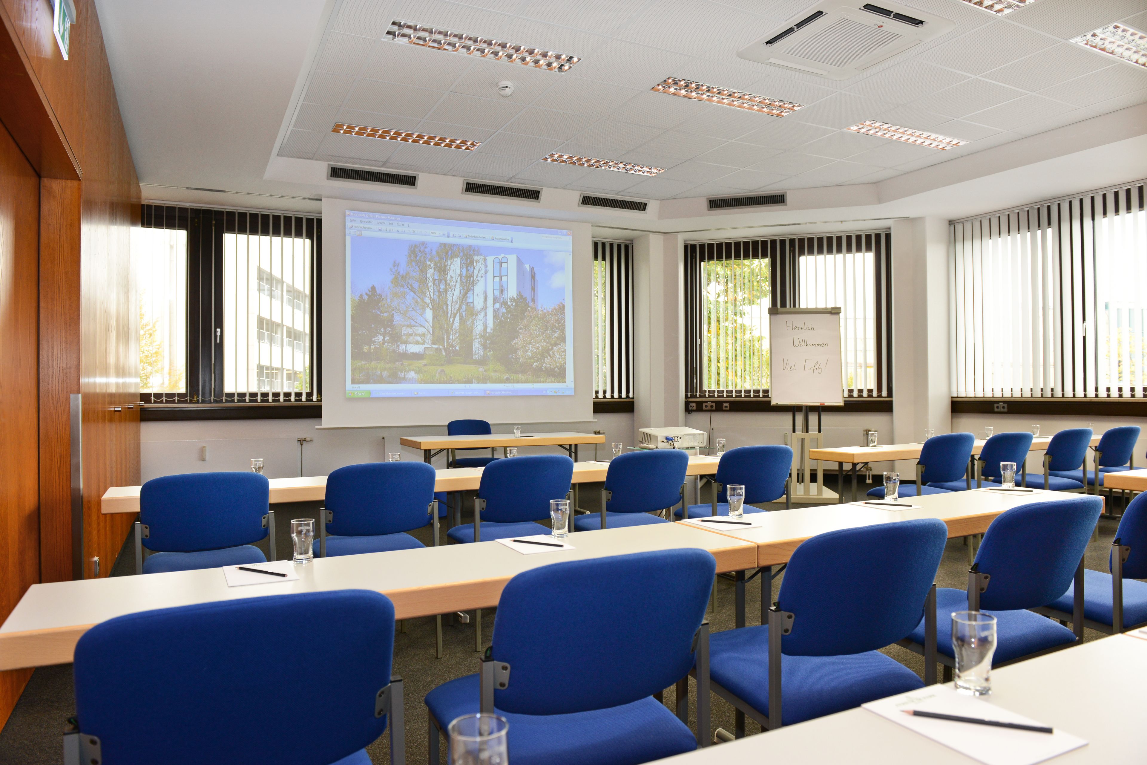 Un salón de conferencias con sillas azules, una pantalla de proyector y una pizarra.