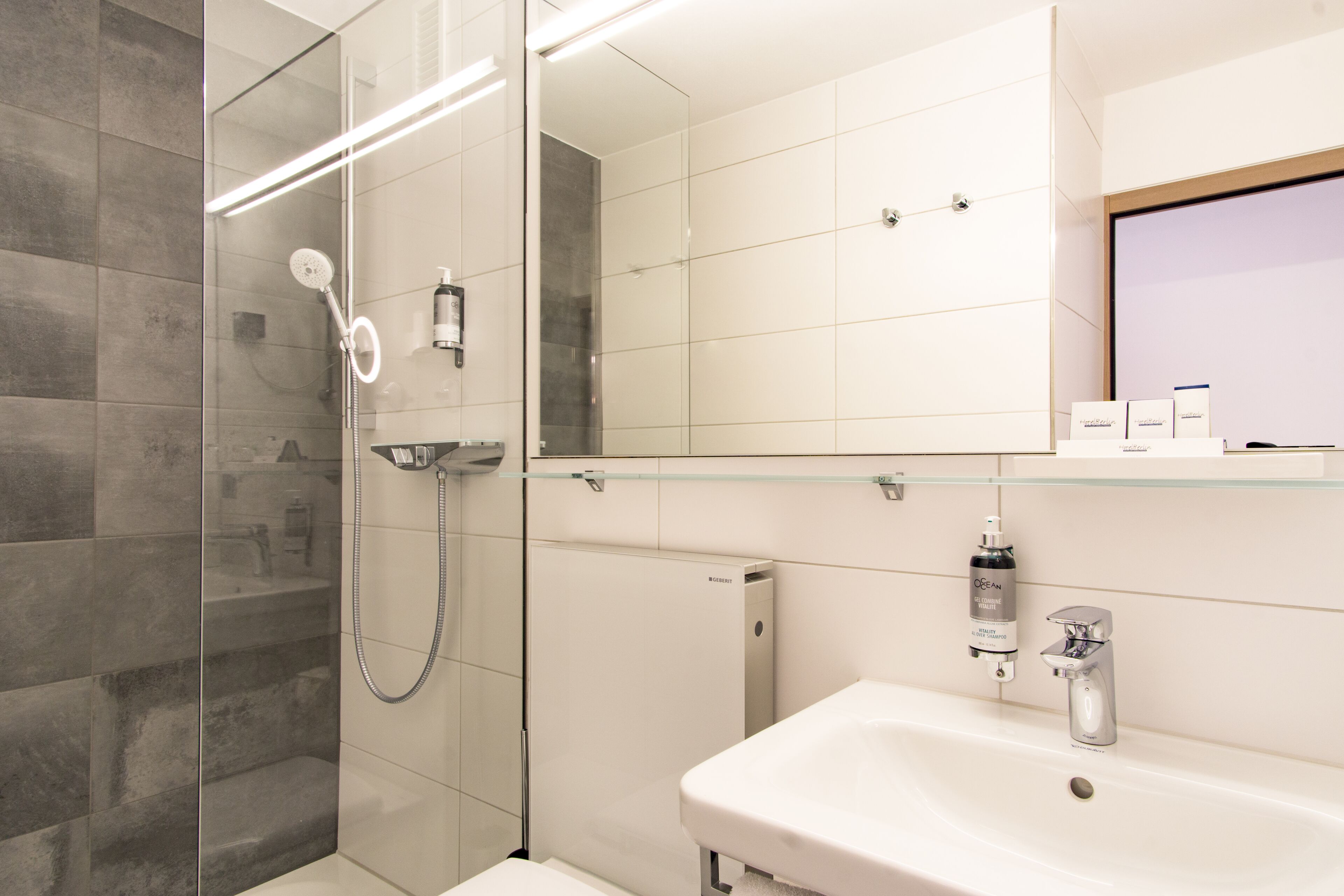 Ein modernes Badezimmer mit einer Duschkabine, einem weißen Waschbecken und einem Spiegel darüber.