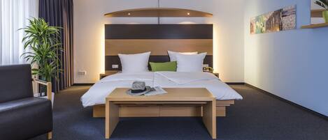 A modern hotel room with a bed, bedside table, and a potted plant.