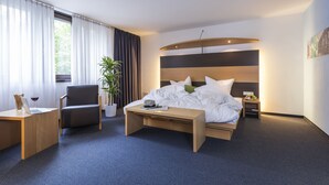 A modern hotel room with a bed, a desk, a chair, a bedside table, and a potted plant. - Hotel Berlin (Sindelfingen)