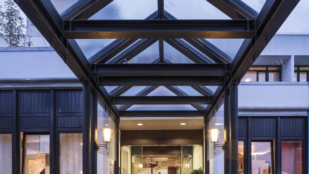 A hotel entrance with a glass canopy, a reception desk, and a visible interior with a counter and seating area. - Hotel Berlin (Sindelfingen)