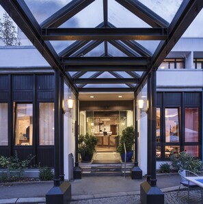A hotel entrance with a glass canopy, a reception desk, and a visible interior with a counter and seating area. - Hotel Berlin (Sindelfingen)
