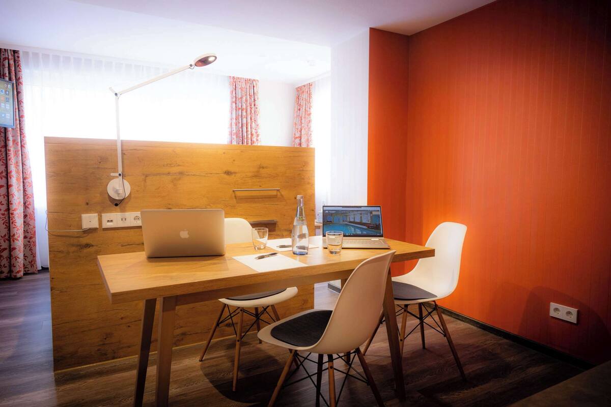 Une chambre moderne avec un bureau en bois, deux chaises, un ordinateur portable, une lampe et une fenêtre avec des rideaux.