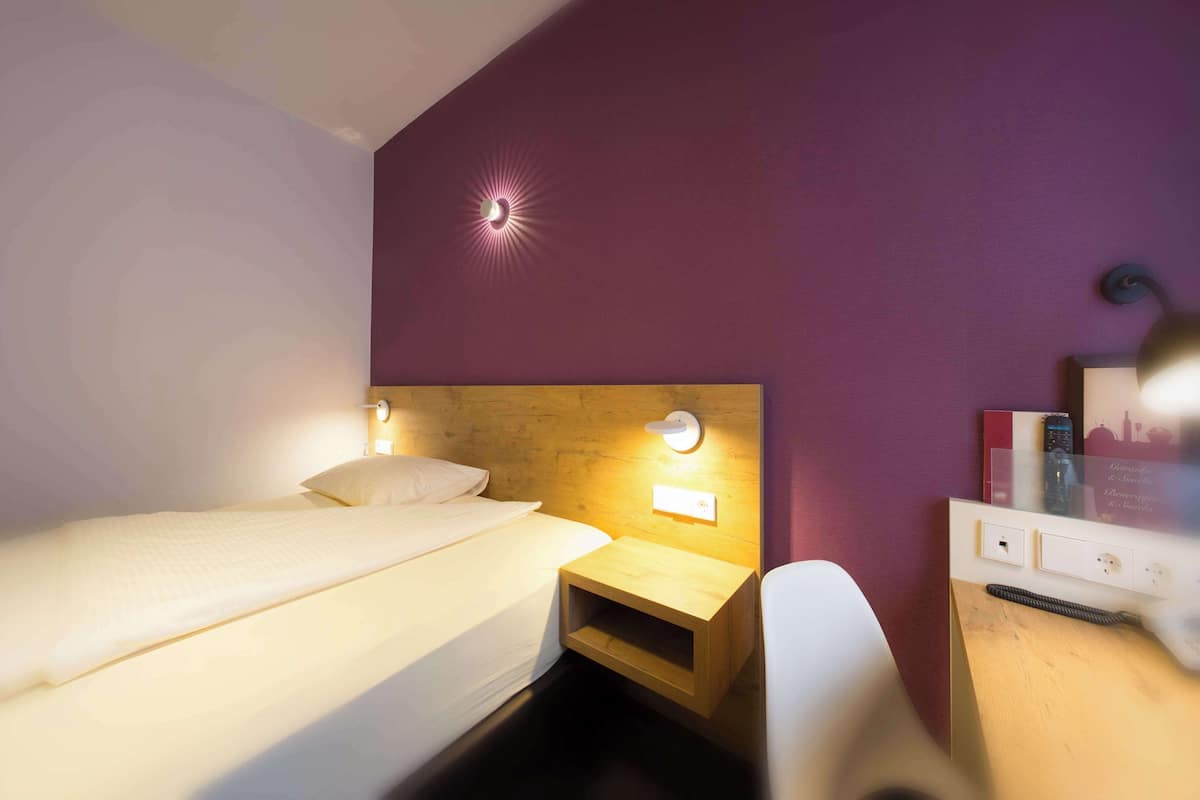 Une chambre d’hôtel comprenant un lit, une table de chevet et un bureau avec une chaise.