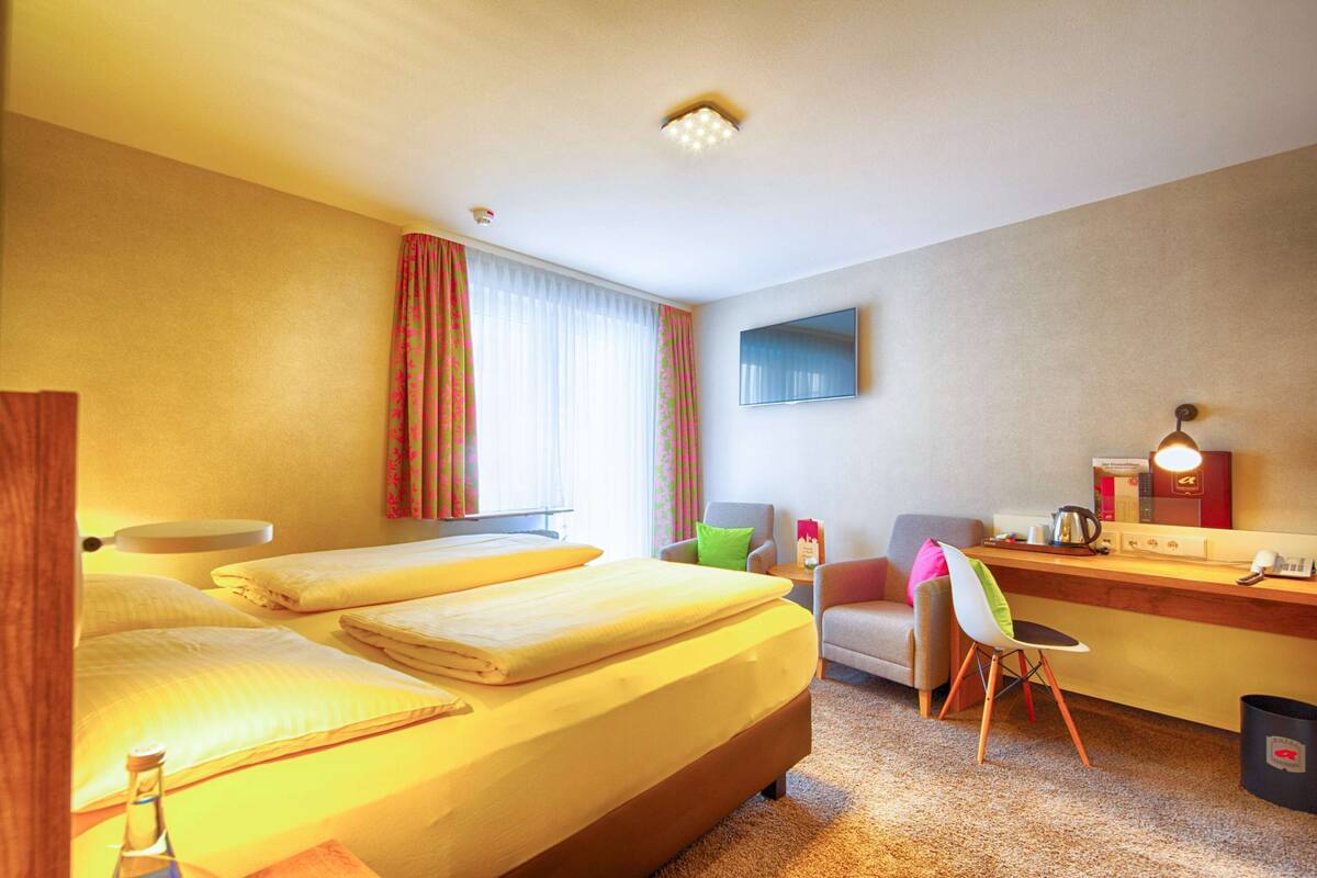 Une chambre d’hôtel équipée d’un lit, d’un bureau, d’une chaise, d’une télévision et d’une fenêtre avec des rideaux.