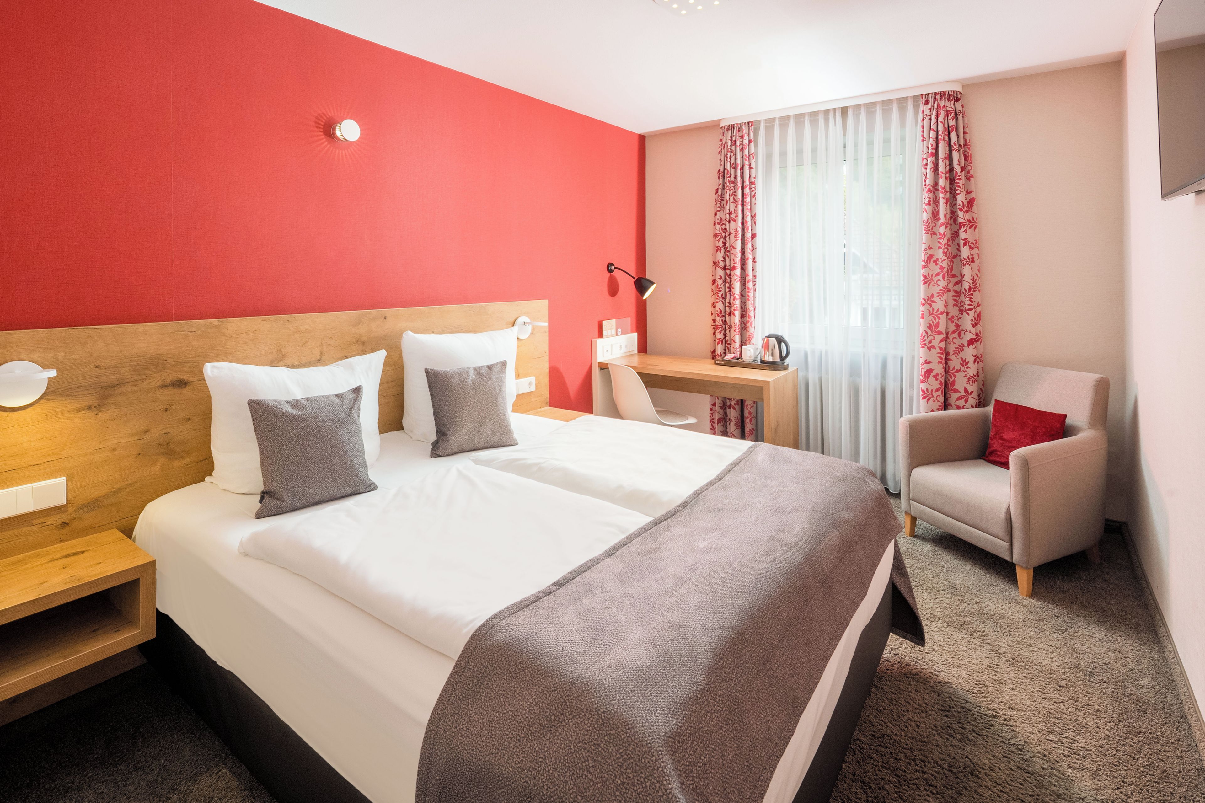 A hotel room with a large bed, a desk, a chair, and a window with curtains.