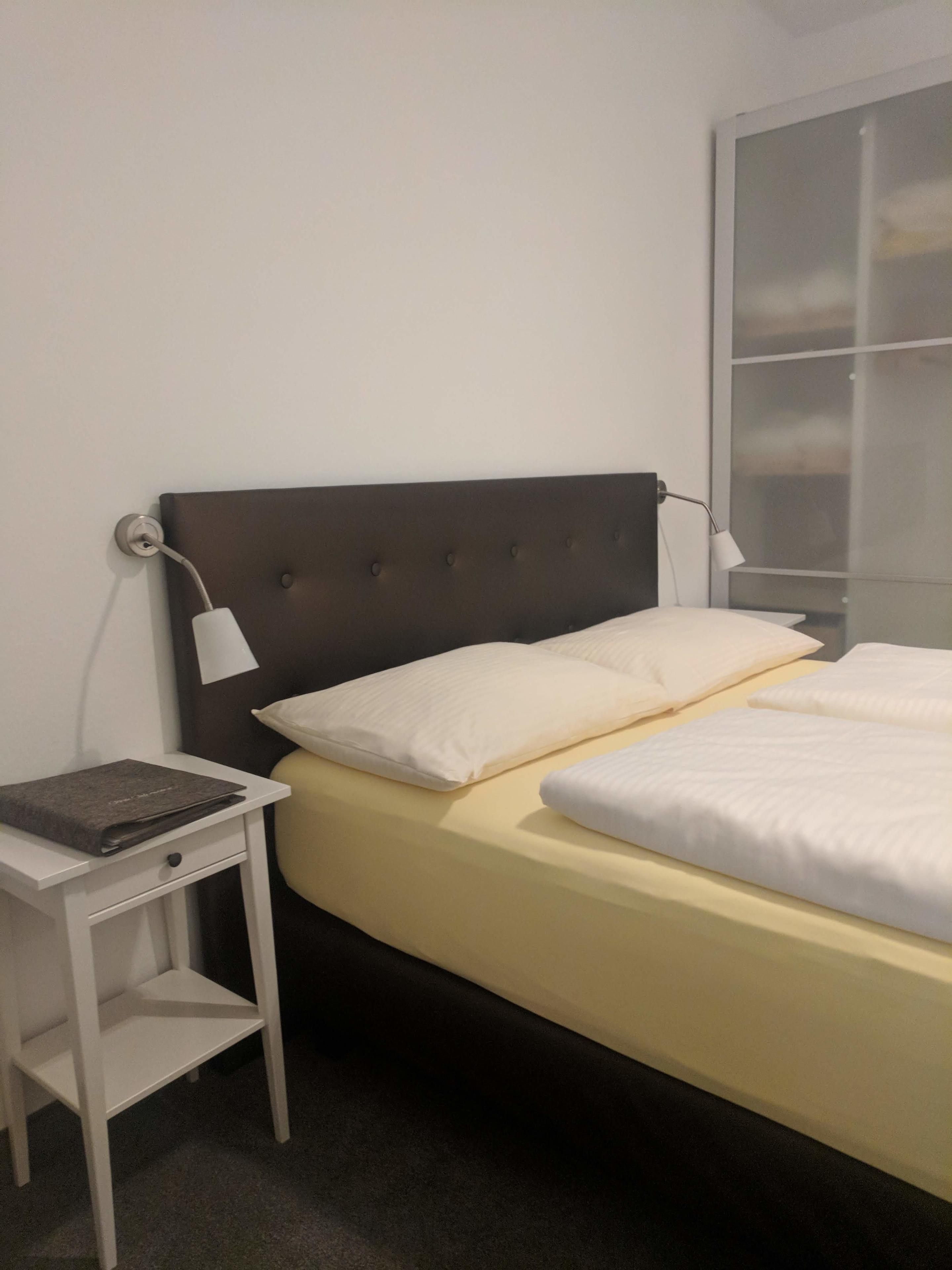 A bed with a headboard, a bedside table with a lamp, and a window with blinds.