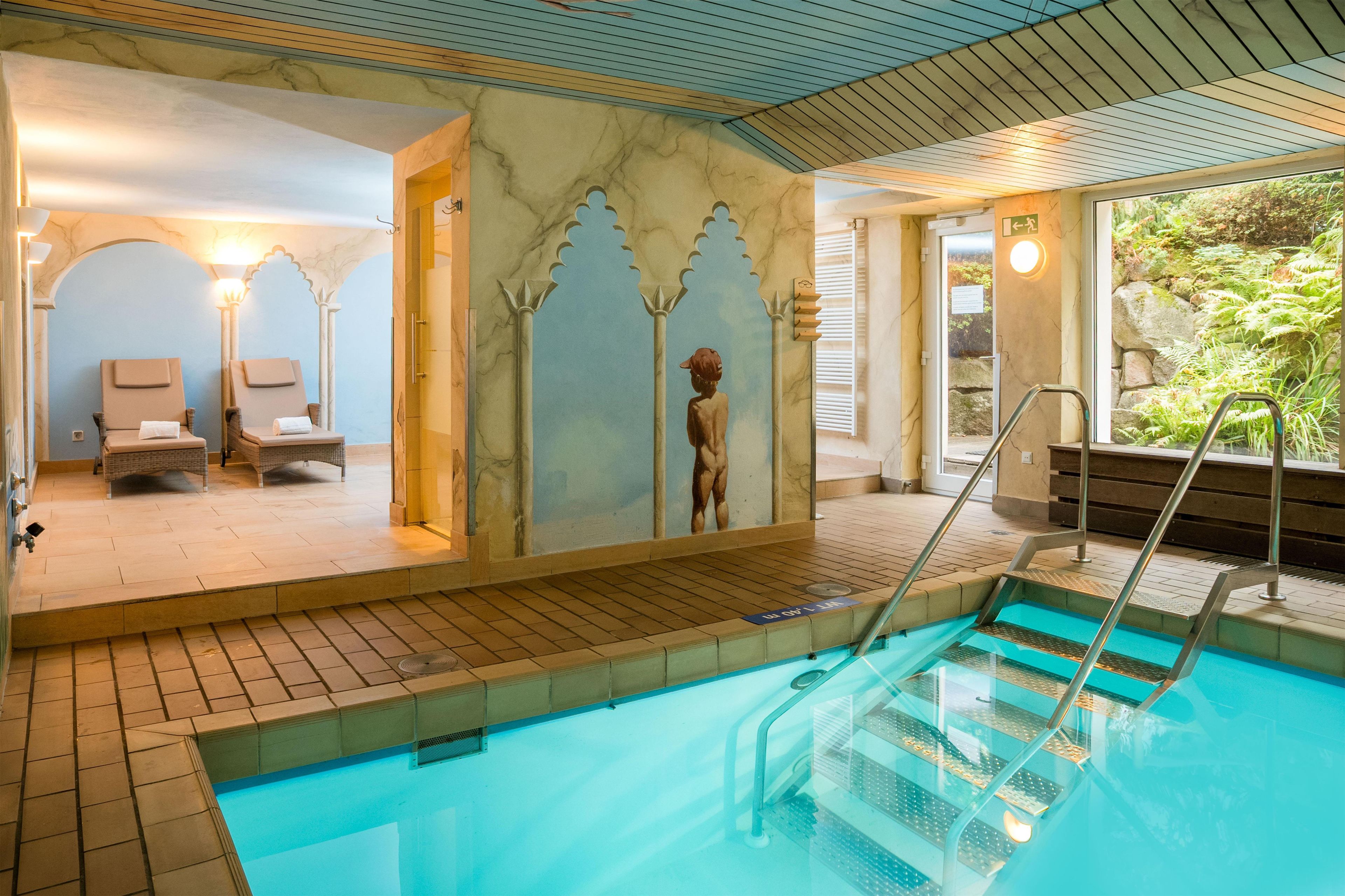 An indoor swimming pool with a clear view of the pool area, a lounge with chairs, and a mural on the wall.