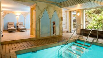 An indoor swimming pool with a clear view of the pool area, a lounge with chairs, and a mural on the wall.