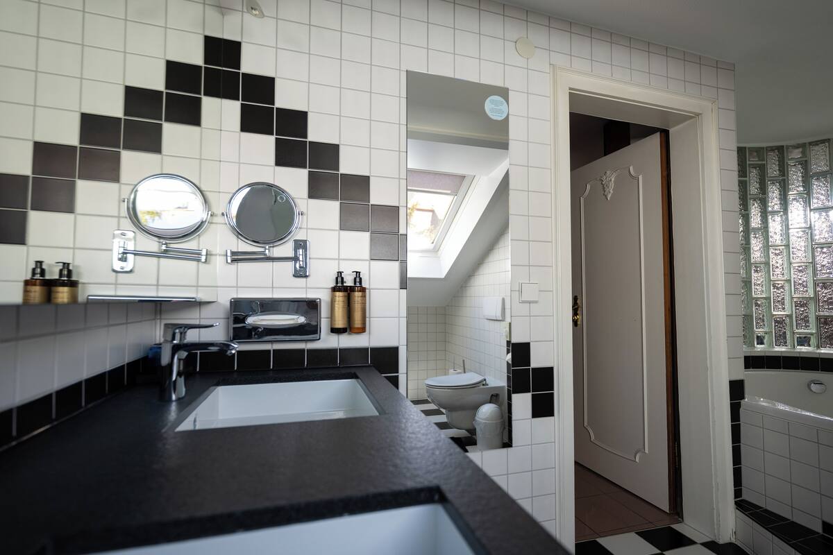 Une salle de bain moderne avec un sol à carreaux noirs et blancs, deux lavabos, des toilettes et une lucarne.