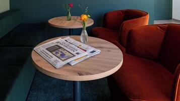 Ein modernes Interieur mit einem runden Holztisch, einem roten Samtsofa und einer Wand mit floralem Muster.