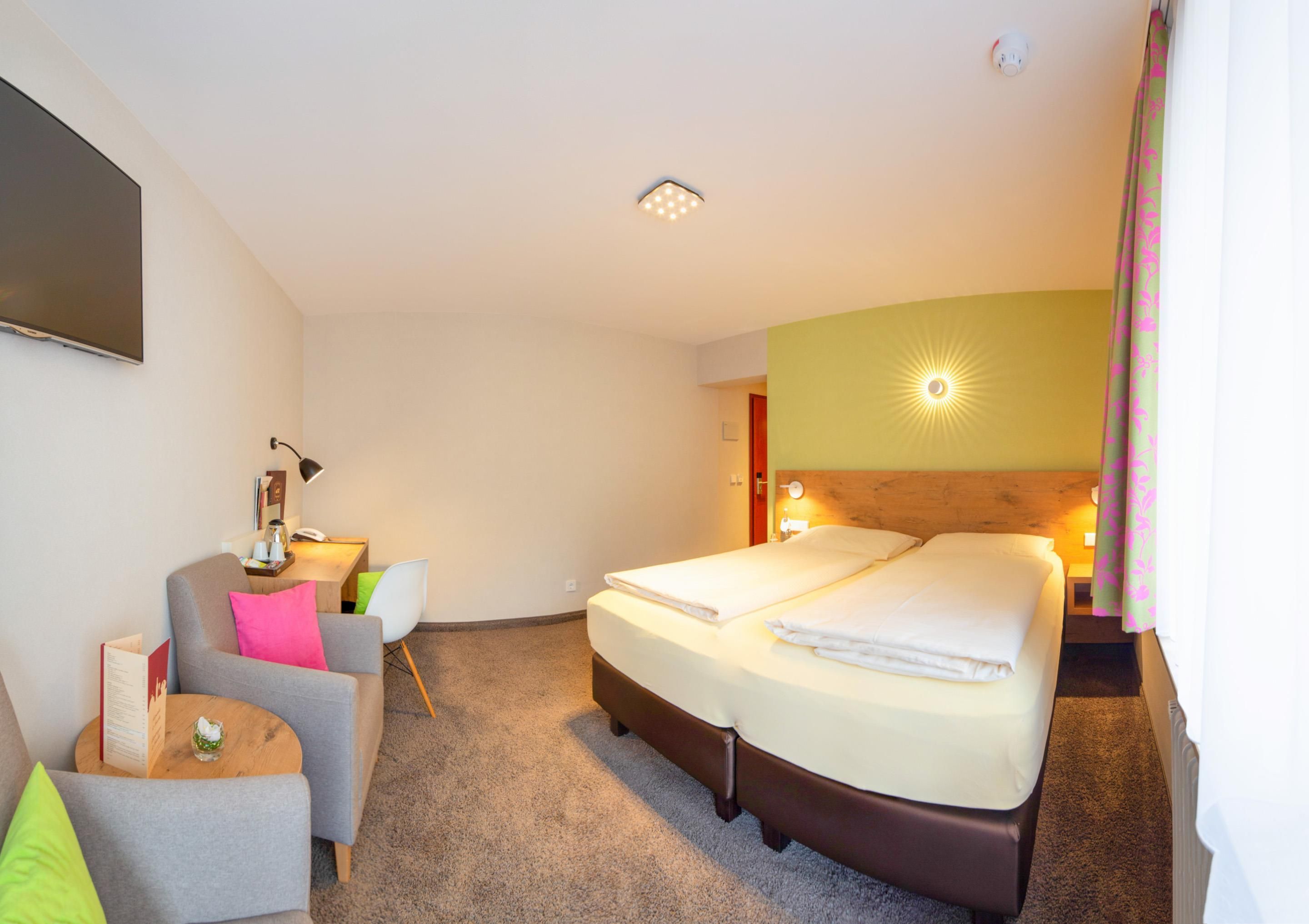 A hotel room with a bed, a desk, a chair, and a television.