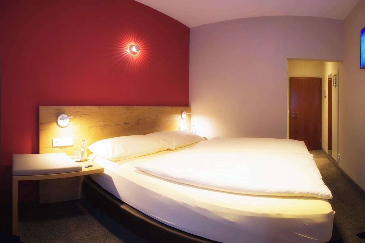 Une chambre d’hôtel avec un grand lit, une table de chevet, une horloge murale et une porte.
