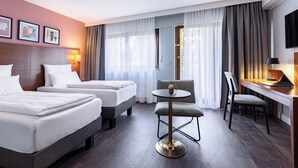 Een hotelkamer met twee bedden, een ronde tafel, een bureau met stoel en een televisie aan de muur.