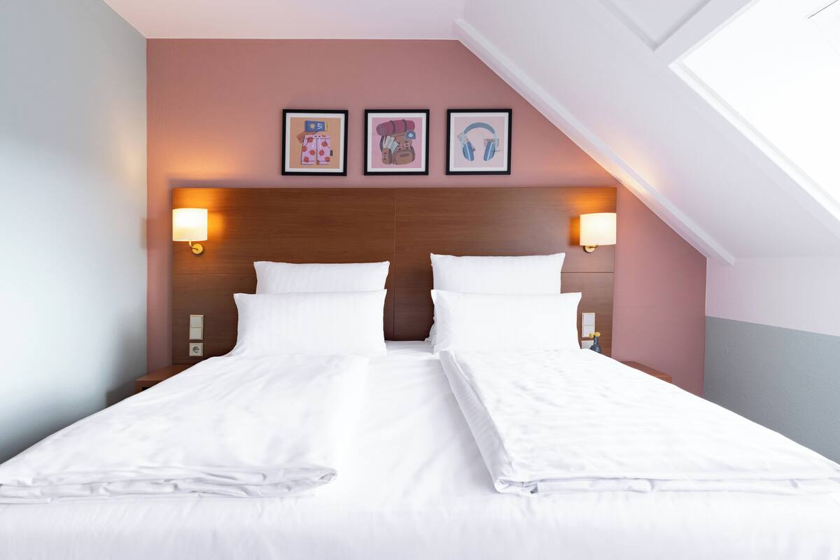 A double bed with white linens, two bedside lamps, and three framed pictures on the wall.
