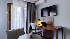 Een moderne hotelkamer met een houten bureau, een laptop, een stoel, een ronde tafel en een aan de muur bevestigde televisie.