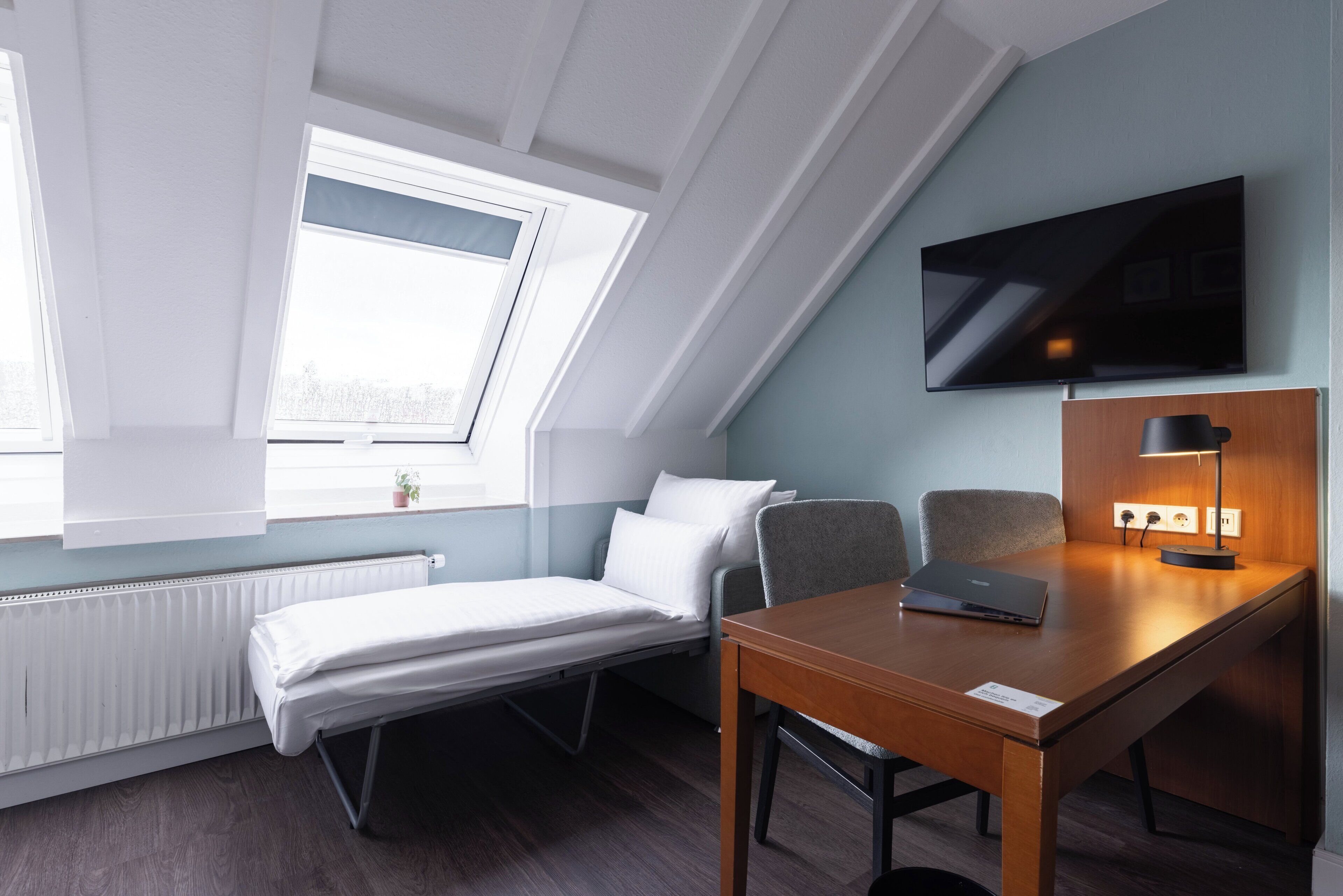 A compact hotel room with a bed, a desk, a chair, a TV, and a window with a view.
