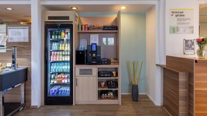 Een hotel receptie met een drankautomaat, een koffieapparaat en een klein aanrecht.